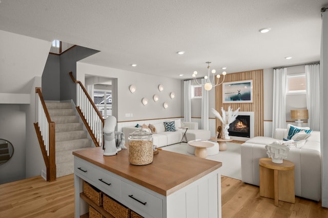 living room with light wood finished floors, a glass covered fireplace, recessed lighting, and stairs