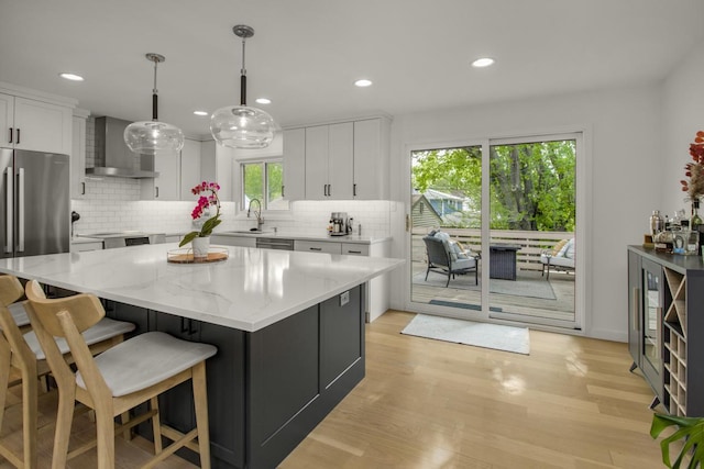 kitchen with wall chimney exhaust hood, a sink, white cabinets, decorative backsplash, and recessed lighting