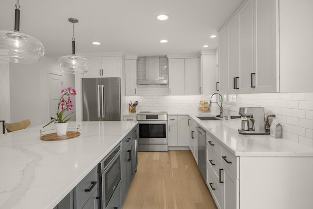 kitchen featuring wall chimney range hood, stainless steel appliances, a sink, white cabinetry, and recessed lighting