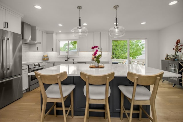 kitchen featuring stainless steel appliances, wall chimney range hood, a sink, light countertops, and a kitchen island