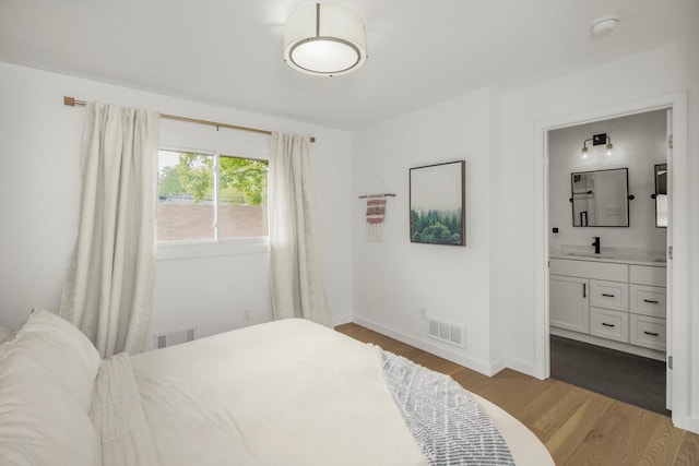bedroom with wood finished floors, a sink, baseboards, and ensuite bathroom