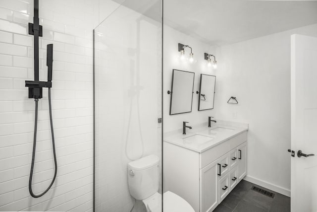 full bathroom with toilet, double vanity, baseboards, and tiled shower