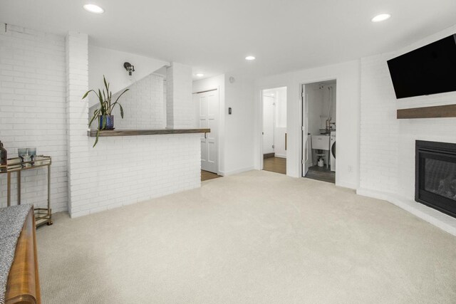 unfurnished living room featuring carpet floors, a glass covered fireplace, recessed lighting, and brick wall