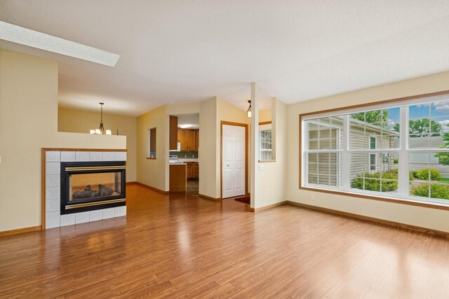 7931 Pinnacle Ave NE, Otsego, MN 55330 - unfurnished living room with wood finished floors, a fireplace, a chandelier, vaulted ceiling, and a skylight