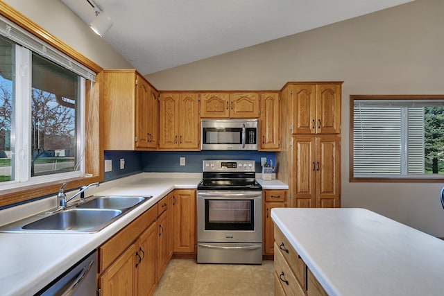 kitchen with light tile patterned flooring, appliances with stainless steel finishes, a sink, light countertops, and vaulted ceiling