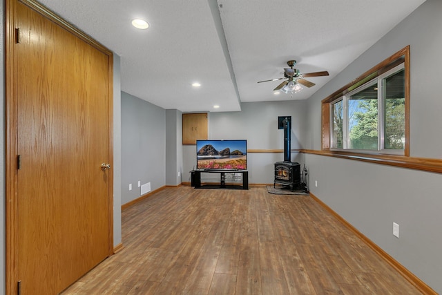 unfurnished living room with ceiling fan, visible vents, a wood stove, hardwood / wood-style flooring, and baseboards
