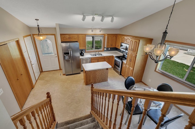 kitchen with appliances with stainless steel finishes, a sink, light countertops, a kitchen island, and pendant lighting