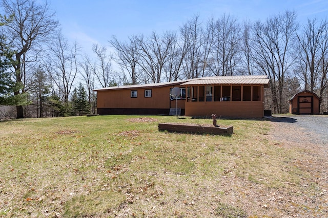 view of front of property featuring an outdoor structure, a front lawn, a storage unit, a sunroom, and metal roof