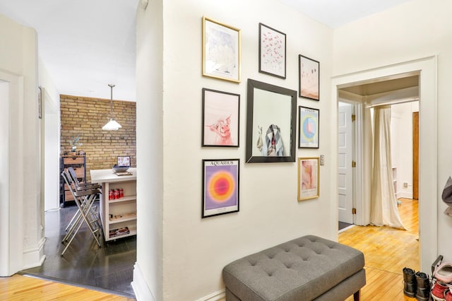hallway with brick wall, wood finished floors, and baseboards
