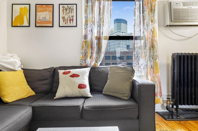living area with radiator heating unit, wood finished floors, an AC wall unit, and a city view