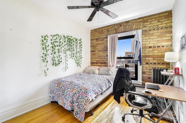bedroom featuring radiator, wood finished floors, an office area, baseboards, and ceiling fan