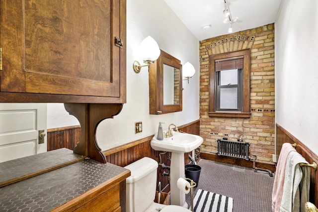 bathroom with a wainscoted wall, wooden walls, track lighting, toilet, and radiator