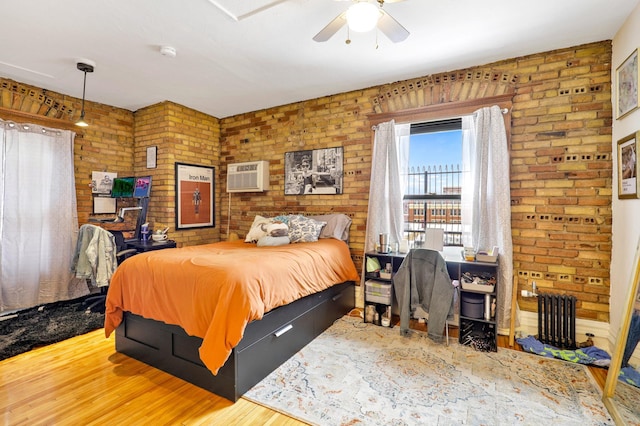 bedroom with wood finished floors, an AC wall unit, brick wall, and radiator heating unit