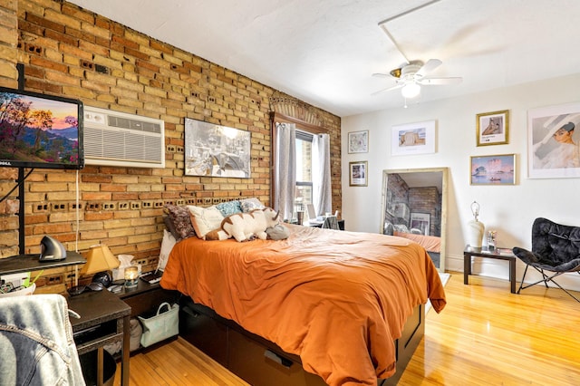 bedroom with wood finished floors, brick wall, a wall mounted AC, and baseboards