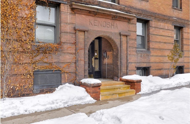 snow covered property entrance with brick siding