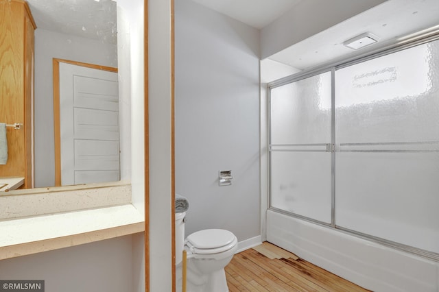 full bathroom featuring vanity, bath / shower combo with glass door, baseboards, wood-type flooring, and toilet