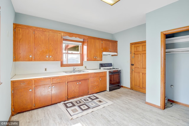 kitchen with a sink, light wood-style floors, gas range oven, light countertops, and under cabinet range hood
