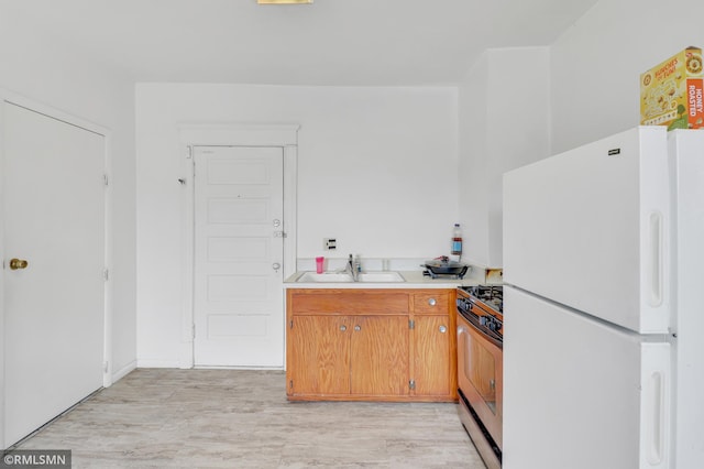 kitchen with a sink, light wood-style floors, light countertops, stainless steel range with gas stovetop, and freestanding refrigerator