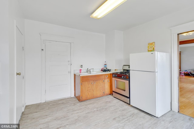 kitchen featuring a sink, freestanding refrigerator, light wood-style floors, light countertops, and stainless steel gas range oven