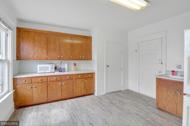 kitchen with brown cabinetry, light wood-style flooring, light countertops, and white microwave
