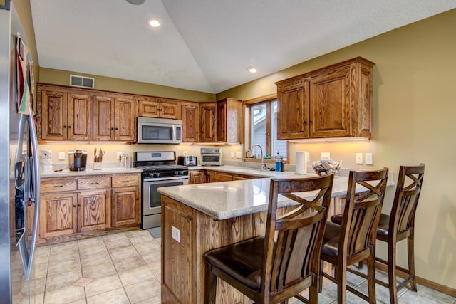 kitchen with stainless steel appliances, vaulted ceiling, visible vents, a peninsula, and brown cabinetry