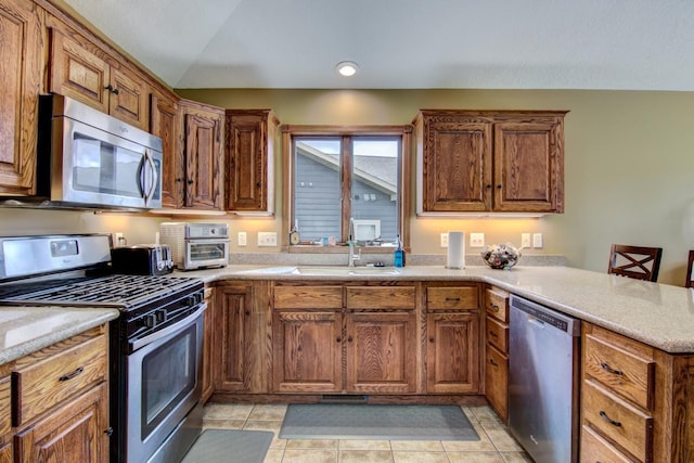 kitchen featuring a peninsula, brown cabinets, stainless steel appliances, and a sink