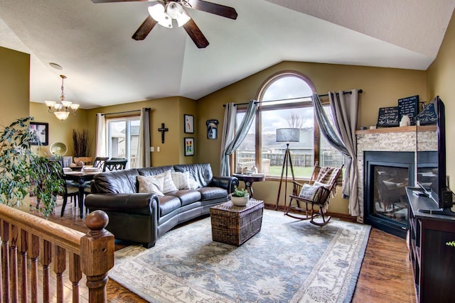 living room featuring vaulted ceiling, a tile fireplace, wood finished floors, and ceiling fan with notable chandelier