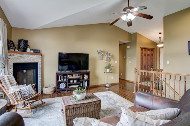 living room with vaulted ceiling, a ceiling fan, wood finished floors, a glass covered fireplace, and baseboards