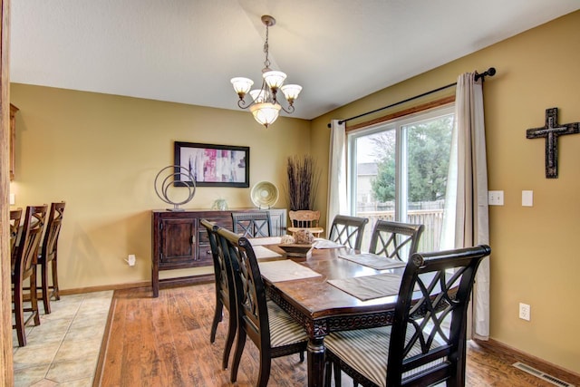 dining area with light wood-type flooring, baseboards, visible vents, and an inviting chandelier