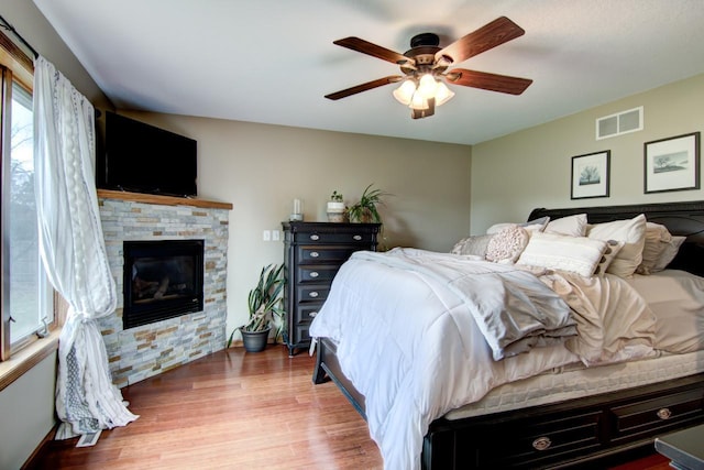 bedroom with wood finished floors, visible vents, a ceiling fan, baseboards, and a fireplace