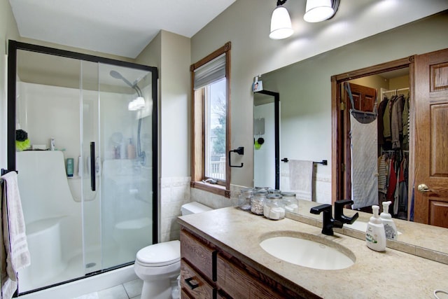 bathroom featuring tile patterned floors, toilet, a stall shower, a spacious closet, and vanity