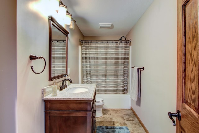 bathroom with stone finish floor, toilet, vanity, shower / bath combo with shower curtain, and baseboards