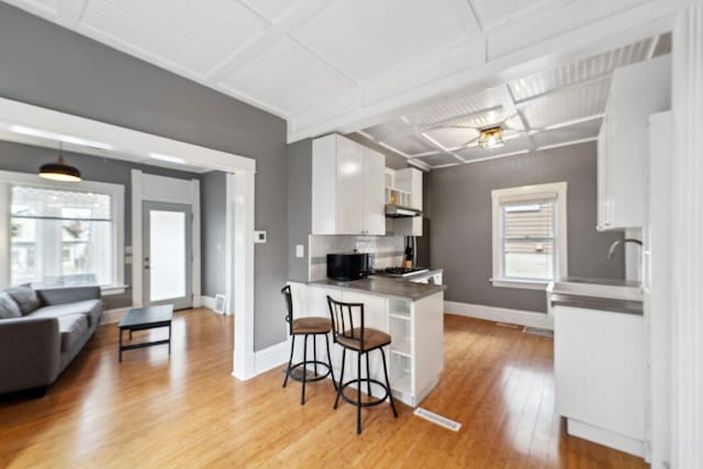 2943 Taylor St NE, Minneapolis, MN 55418 - kitchen with a breakfast bar, baseboards, wall chimney range hood, white cabinetry, and light wood-style flooring