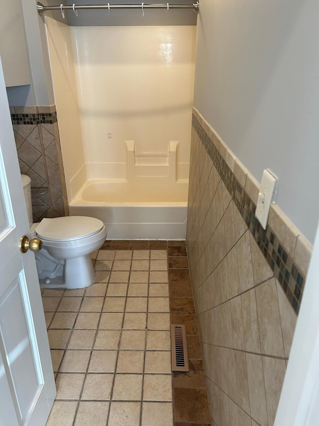 bathroom with wainscoting, toilet, tile walls, shower / bathing tub combination, and visible vents
