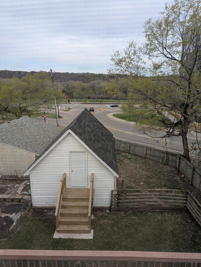 back of property featuring fence, an outbuilding, and a shingled roof