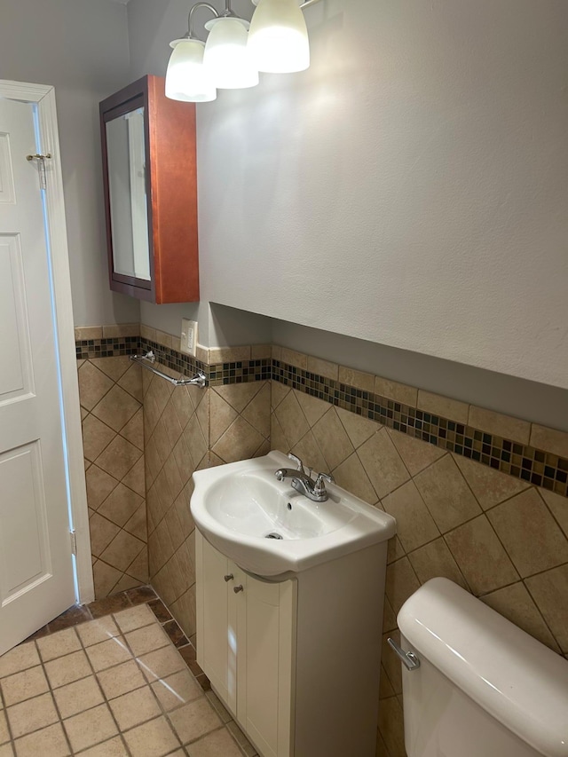bathroom with tile walls, a wainscoted wall, vanity, and toilet