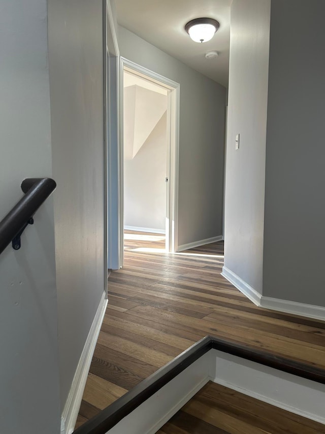 corridor with dark wood-type flooring, baseboards, and an upstairs landing