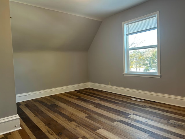 additional living space with baseboards, vaulted ceiling, dark wood-style floors, and visible vents