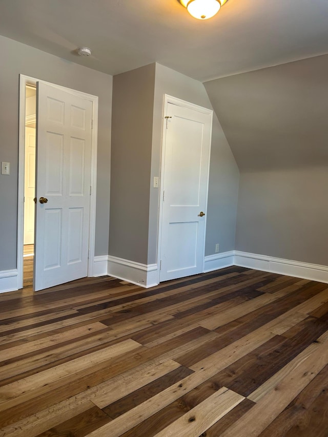 additional living space with baseboards, dark wood finished floors, and lofted ceiling