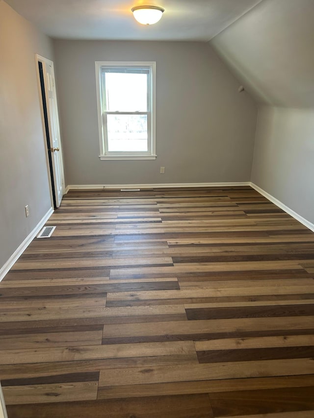 additional living space with baseboards, dark wood-style flooring, vaulted ceiling, and visible vents