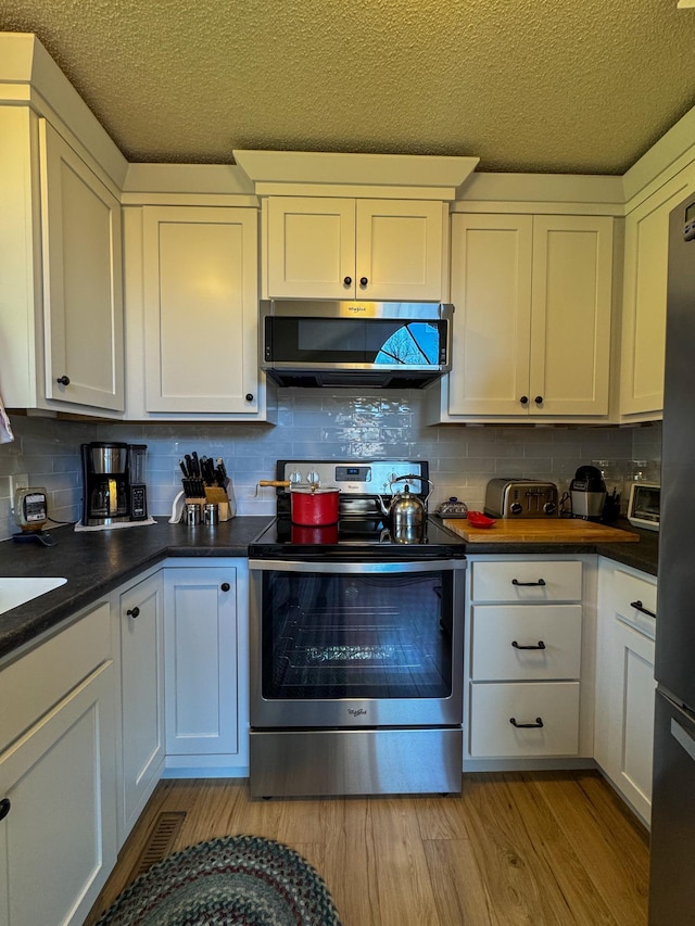 17783 Lookout Tower Rd NE, Hines, MN 56647 - kitchen with appliances with stainless steel finishes, dark countertops, white cabinetry, tasteful backsplash, and light wood finished floors
