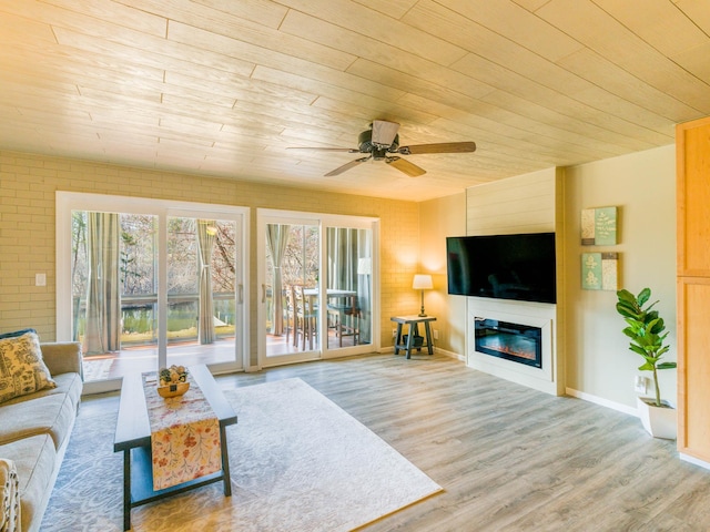 living area featuring wood ceiling, wood finished floors, a glass covered fireplace, and ceiling fan