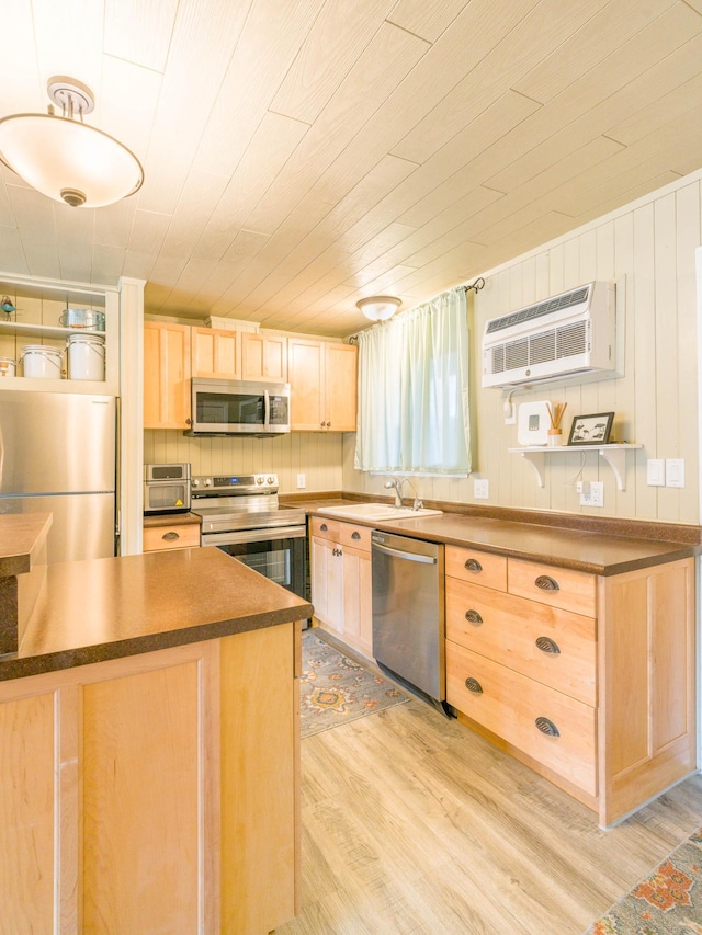 kitchen with light brown cabinets, dark countertops, a sink, stainless steel appliances, and light wood finished floors