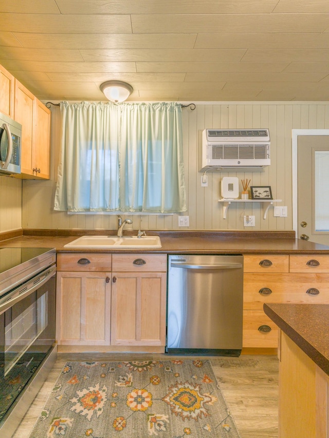 kitchen with an AC wall unit, a sink, light brown cabinetry, light wood-type flooring, and appliances with stainless steel finishes