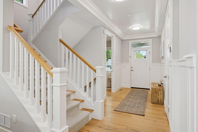 entrance foyer featuring light wood-style floors, a wainscoted wall, ornamental molding, and stairway
