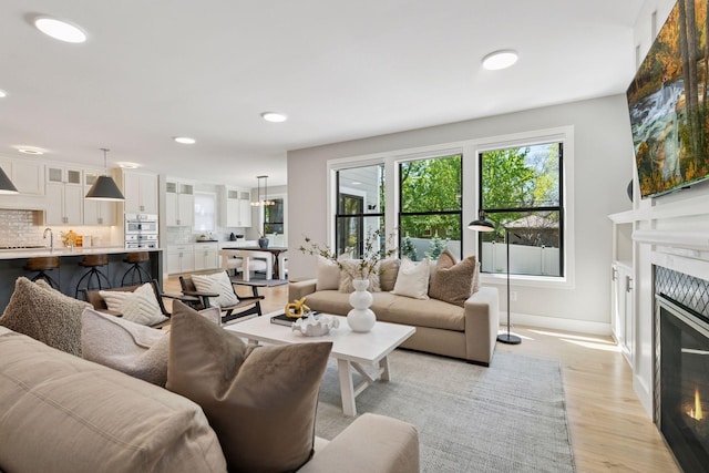 living room featuring a glass covered fireplace, light wood-type flooring, plenty of natural light, baseboards, and recessed lighting