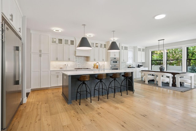 kitchen featuring stainless steel appliances, light wood finished floors, decorative backsplash, light countertops, and white cabinets