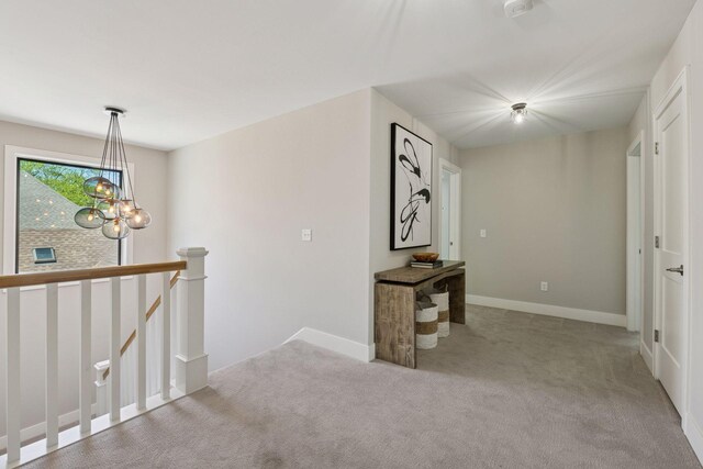 corridor with carpet flooring, an upstairs landing, a chandelier, and baseboards