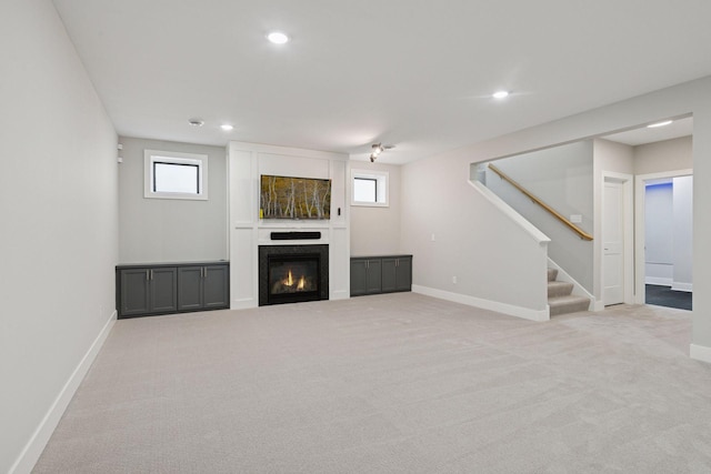unfurnished living room with stairs, carpet, a glass covered fireplace, and recessed lighting