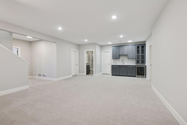 unfurnished living room featuring beverage cooler, light carpet, recessed lighting, baseboards, and a sink